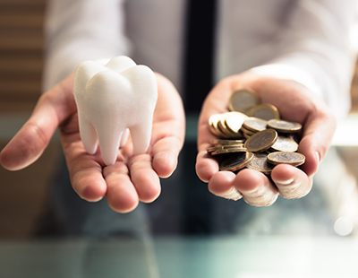 Two hands holding tooth model and coins