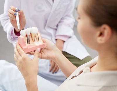 A dentist pointing to a dental implant model 