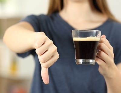 A person holding a cup of coffee in one hand while giving a thumbs-down motion with their other hand