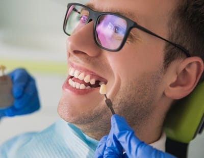 A dentist using a shade guide to determine the correct color of a dental implant for a male patient with a missing tooth
