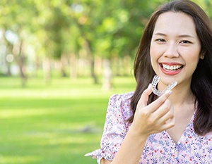 Woman holding clear aligner outside and smiling