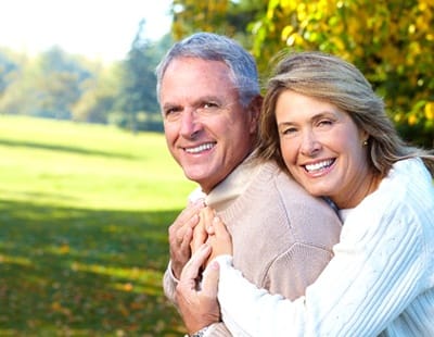 An older couple smiling and hugging outside.