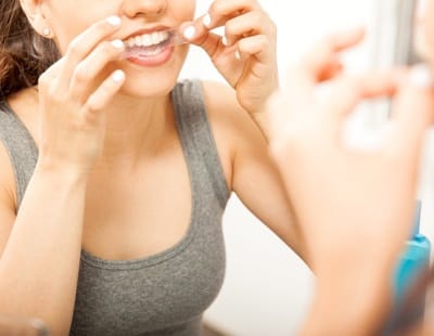 A young female admires her new smile in the mirror that is being held by a dental hygienist