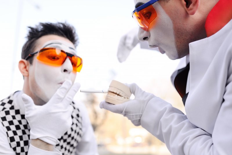 Two mimes holding a model of a set of teeth with a cigarette clenched in between them