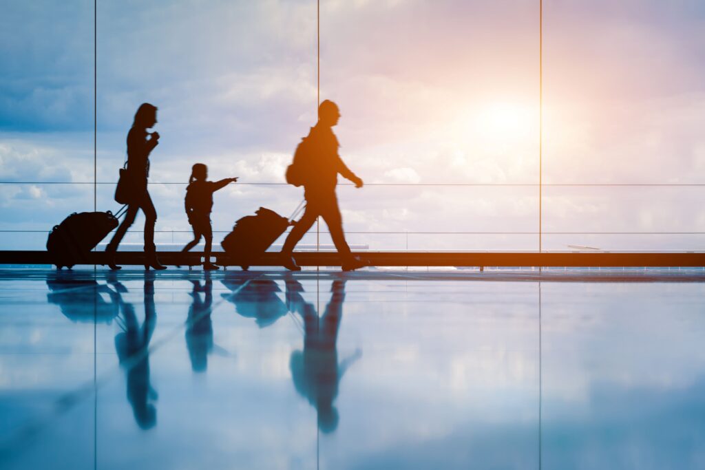 Family crossing expansive glass window with luggage at airport