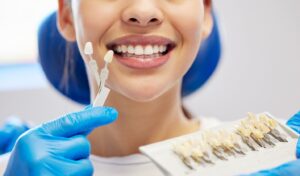 Veneers being held up by gloved hand in front of smiling dental patient.